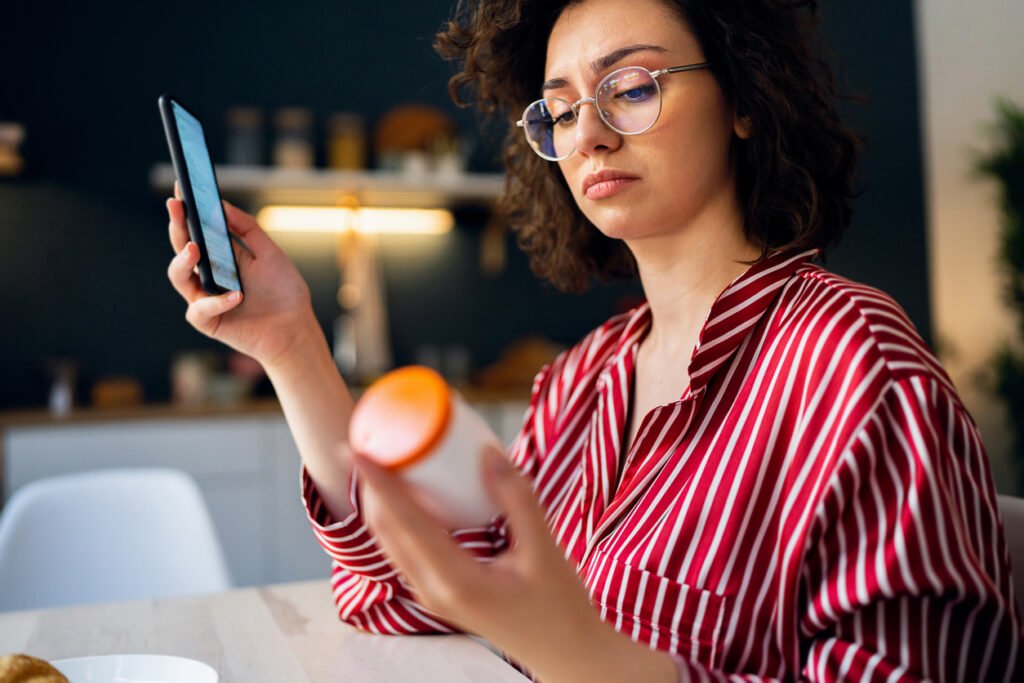 Mulher segurando frasco de remédio e celular
