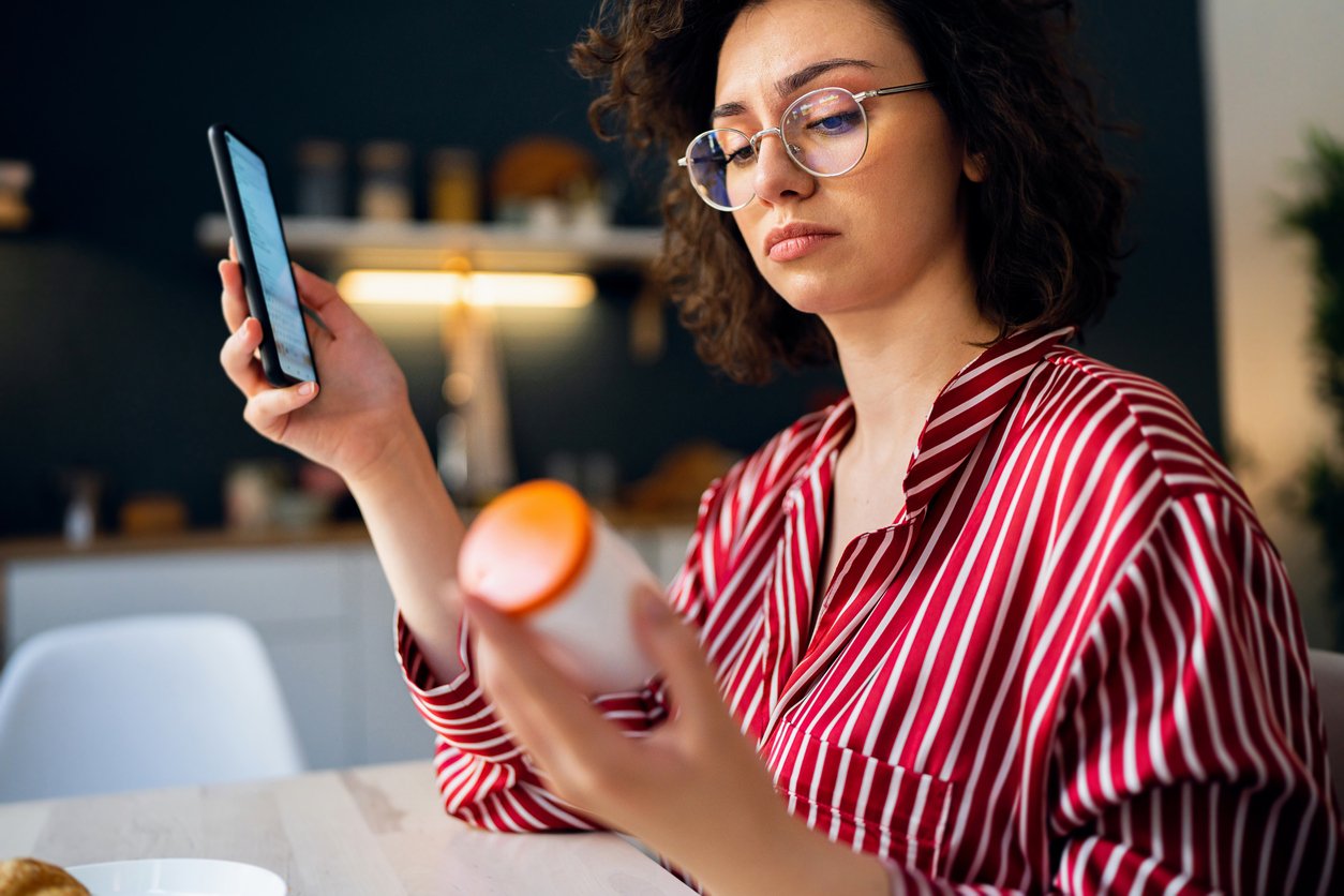 Mulher segurando frasco de remédio e celular
