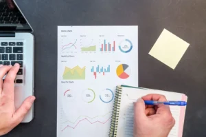 Pessoa planejando orçamento de artigo patrocinado com gráficos, anotações e notebook sobre a mesa